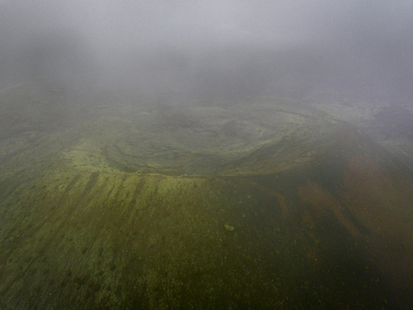 Aerial view of the volcanic crater in Lanzarote featuring rugged slopes mossy textures and a misty overcast sky in Lanzarote Canarias Spain. Aerial view of the volcanic crater in Lanzarote featuring rugged slopes mossy textures and a misty overcast sky in Lanzarote Canarias Spain.