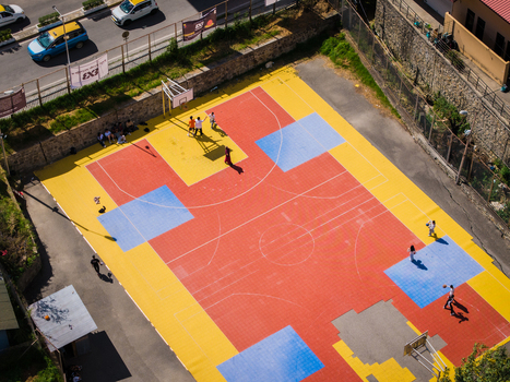 Aerial view of the vibrant red and yellow basketball court where players cast long shadows in the afternoon sun Thimphu Bhutan.