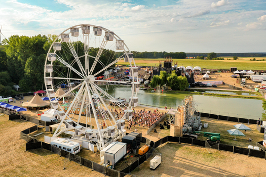 Herzogenaurach Germany 22 July 2022 Aerial view of Open Beatz Festival featuring a large white Ferris wheel festival stages and crowds of people in the green fields of Bayern. Herzogenaurach Germany 22 July 2022 Aerial view of Open Beatz Festival featuring a large white Ferris wheel festival stages and crowds of people in the green fields of Bayern.