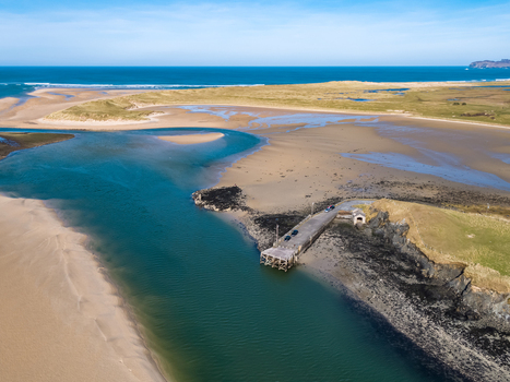 Aerial view of Ballyness Bay featuring a small pier extending into the tidal waters with expansive sandbanks and coastal dunes in Ballyness County Donegal Ireland. Aerial view of Ballyness Bay featuring a small pier extending into the tidal waters with expansive sandbanks and coastal dunes in Ballyness County Donegal Ireland.