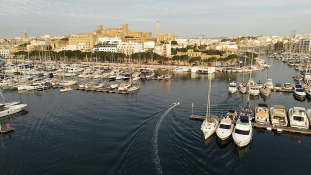 Aerial view of Msida Marina filled with numerous yachts and boats with a small motorboat creating a wake in the calm water set against the urban skyline of Malta. Aerial view of Msida Marina filled with numerous yachts and boats with a small motorboat creating a wake in the calm water set against the urban skyline of Malta.