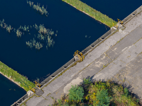 Aerial view of a coal mine settling pond with dark water concrete embankment yellow safety railings and surrounding vegetation in Jaworzno Silesian Voivodeship Poland.