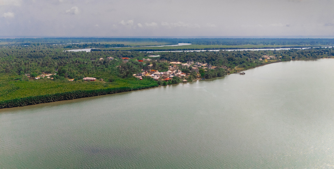 Aerial view of a small village nestled among dense mangroves and lush greenery along the banks of a wide river in Minima Rivers Nigeria.