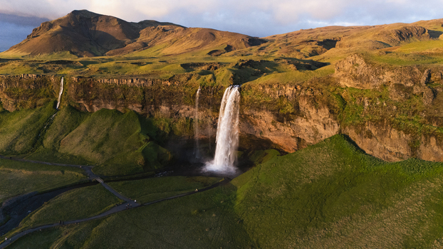 Aerial view of the majestic Seljalandsfoss waterfall cascading over rugged cliffs its white waters contrasting against the verdant green landscape at midnight sun Seljalandsfoss Iceland. Aerial view of the majestic Seljalandsfoss waterfall cascading over rugged cliffs its white waters contrasting against the verdant green landscape at midnight sun Seljalandsfoss Iceland.