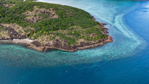 Aerial view of Haslewood Island featuring lush green vegetation rocky coastal cliffs and vibrant turquoise coral reef waters in the Whitsundays Queensland Australia. Aerial view of Haslewood Island featuring lush green vegetation rocky coastal cliffs and vibrant turquoise coral reef waters in the Whitsundays Queensland Australia.