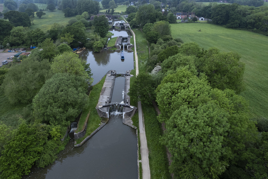 Aerial view of Hatton Locks on the Grand Union Canal featuring historic canal locks surrounded by lush green fields trees and a narrow towpath in Hatton England United Kingdom. Aerial view of Hatton Locks on the Grand Union Canal featuring historic canal locks surrounded by lush green fields trees and a narrow towpath in Hatton England United Kingdom.