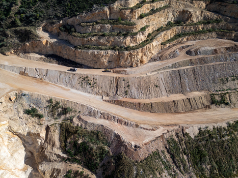 Aerial view of an open pit quarry with terraced rock walls dirt roads and heavy machinery operating in Teulada Valencian Community Spain.