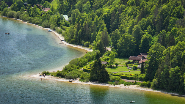 Aerial view of the serene Lac de Joux s shoreline where emerald waters meet verdant forests and quaint settlements nestle peacefully Le Lieu Vaud Switzerland.
