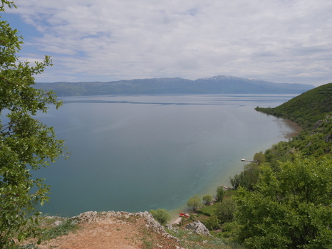 View of Lake Ohrid from the village of Lin with rocky terrain lush green trees and distant mountains under a cloudy sky in Lin Korce County Albania.
