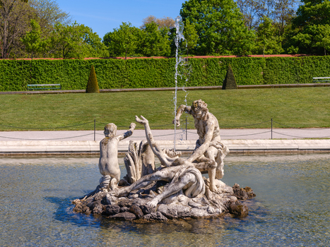 View of the baroque fountain sculptures in the gardens of Belvedere Palace with green hedges and lush trees under a clear blue sky in Vienna Austria. View of the baroque fountain sculptures in the gardens of Belvedere Palace with green hedges and lush trees under a clear blue sky in Vienna Austria.