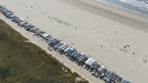 Aerial view of a long row of beach houses situated between grassy dunes and the sandy shoreline of the North Sea in Velsen Noord Noord Holland Netherlands.