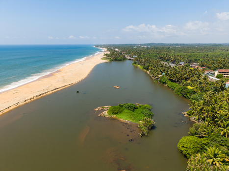 Aerial view of the coastline where a river meets the ocean featuring a sandy beach lush palm forests and a small green island in Galle Southern Province Sri Lanka.