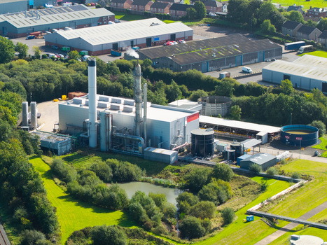 Aerial view of an industrial wastewater treatment facility with storage tanks and processing buildings surrounded by lush green trees and nearby warehouses in Lisburn Northern Ireland United Kingdom.
