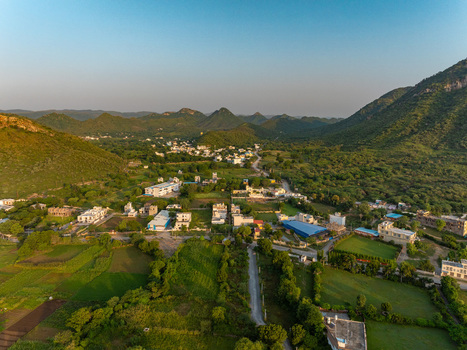 Aerial view of a village nestled in the Aravalli hills near Udaipur featuring scattered houses green fields and winding roads in Udaipur Rajasthan India.
