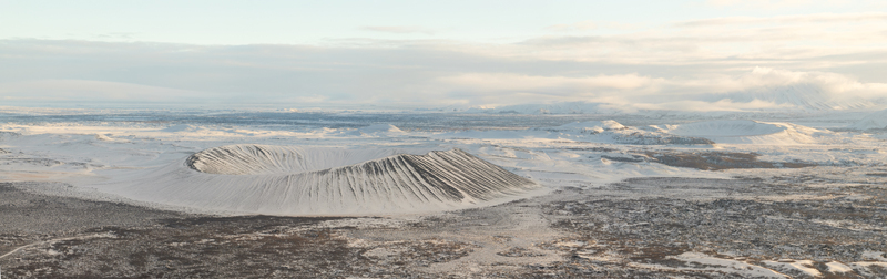 Aerial view of the Hverfjall volcanic crater covered in snow surrounded by a vast desolate volcanic landscape under a soft sky in Thingeyjarsveit Iceland.