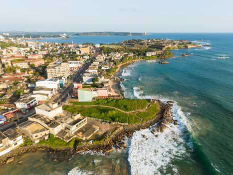 Aerial view of the coastal city with urban buildings and turquoise ocean waves crashing on the shore near the historic Galle Fort in Galle Southern Province Sri Lanka.