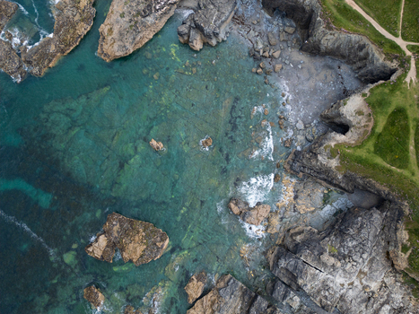 Aerial view of the rugged cliffs and turquoise water at Godrevy Beach with rocky shoreline and green coastal paths in Gwithian England United Kingdom. Aerial view of the rugged cliffs and turquoise water at Godrevy Beach with rocky shoreline and green coastal paths in Gwithian England United Kingdom.
