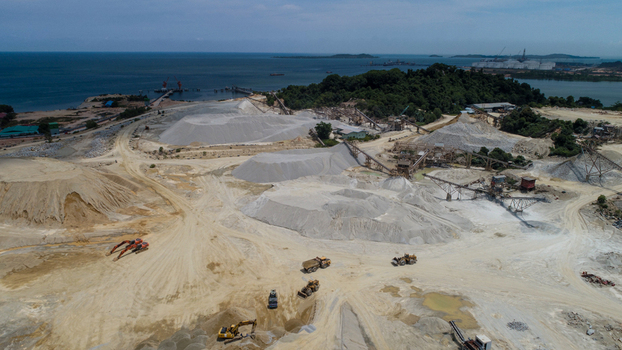 Aerial view of a large scale sand mining operation with heavy machinery piles of sand and conveyor systems located along the coast in Karimun Kepulauan Riau Indonesia. Aerial view of a large scale sand mining operation with heavy machinery piles of sand and conveyor systems located along the coast in Karimun Kepulauan Riau Indonesia.