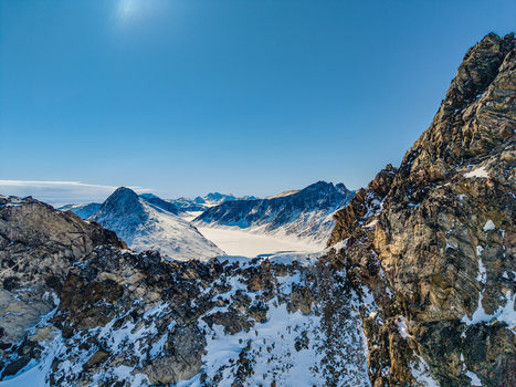 Aerial view of rugged snow covered mountain peaks and a vast frozen glacier valley under a clear blue sky Tasiilaq Sermersooq Municipality Greenland. Aerial view of rugged snow covered mountain peaks and a vast frozen glacier valley under a clear blue sky Tasiilaq Sermersooq Municipality Greenland.