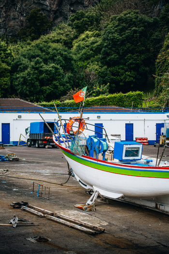 View of a fishing boat adorned with the Portuguese flag sits on a concrete bank against lush green hills a symphony of color and texture São Miguel Portugal. View of a fishing boat adorned with the Portuguese flag sits on a concrete bank against lush green hills a symphony of color and texture São Miguel Portugal.