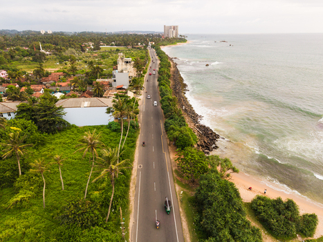 Aerial view of Dadalla beach and the coastal road lined with palm trees and buildings under a cloudy sky in Galle Southern Province Sri Lanka. Aerial view of Dadalla beach and the coastal road lined with palm trees and buildings under a cloudy sky in Galle Southern Province Sri Lanka.