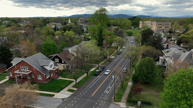 Aerial view of a residential street in spring featuring historic brick houses lush green trees and cars driving along the road with a school building in Lynchburg Virginia United States. Aerial view of a residential street in spring featuring historic brick houses lush green trees and cars driving along the road with a school building in Lynchburg Virginia United States.