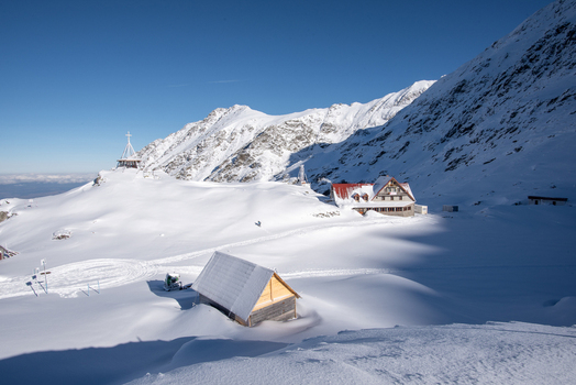 View of the snow covered Balea Lake area with a wooden cabin in the foreground and a mountain lodge nestled against the snowy slopes under a clear blue sky in Cartisoara Sibiu Romania. View of the snow covered Balea Lake area with a wooden cabin in the foreground and a mountain lodge nestled against the snowy slopes under a clear blue sky in Cartisoara Sibiu Romania.
