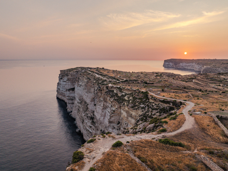Aerial view of rugged sun kissed cliffs meeting the tranquil dark blue sea under a pastel sky at Sanap Cliffs Munxar Gozo Malta. Aerial view of rugged sun kissed cliffs meeting the tranquil dark blue sea under a pastel sky at Sanap Cliffs Munxar Gozo Malta.