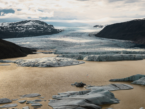 Aerial view of Vatnajokull glacier with floating icebergs in a glacial lagoon and rugged mountains under a cloudy sky in Iceland.