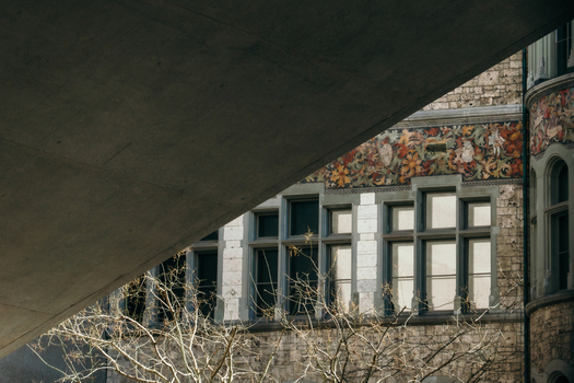 View of the detailed facade of the National Museum with stone walls and colorful floral motifs framed by a stark concrete structure above Zurich Switzerland. View of the detailed facade of the National Museum with stone walls and colorful floral motifs framed by a stark concrete structure above Zurich Switzerland.