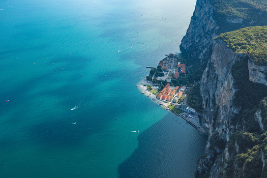 Aerial view of Campione del Garda village nestled beneath towering limestone cliffs on the western shore of Lake Garda Italy.