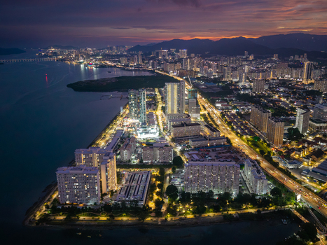 George Town Malaysia 22 September 2026 Aerial view of the George Town cityscape at night featuring illuminated skyscrapers coastal roads and the sea under a twilight sky.