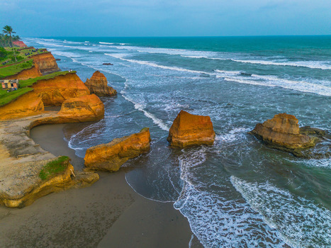 Aerial view of dramatic orange coastal cliffs and rock formations rising from the turquoise ocean waters along the sandy beach in Bali Indonesia. Aerial view of dramatic orange coastal cliffs and rock formations rising from the turquoise ocean waters along the sandy beach in Bali Indonesia.