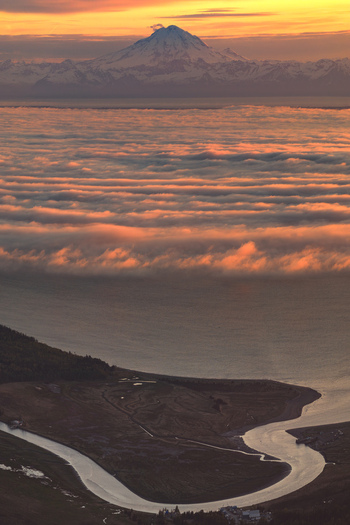 Aerial view of Alaska Wilderness featuring a winding river through the landscape beneath clouds and a distant snow capped mountain at sunset in Palmer Alaska United States. Aerial view of Alaska Wilderness featuring a winding river through the landscape beneath clouds and a distant snow capped mountain at sunset in Palmer Alaska United States.