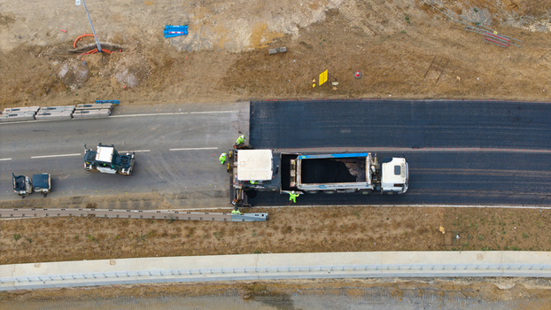 Aerial view of road construction at Black Cat Roundabout with asphalt paving machine dump truck and workers in high visibility gear in Chawston England United Kingdom. Aerial view of road construction at Black Cat Roundabout with asphalt paving machine dump truck and workers in high visibility gear in Chawston England United Kingdom.