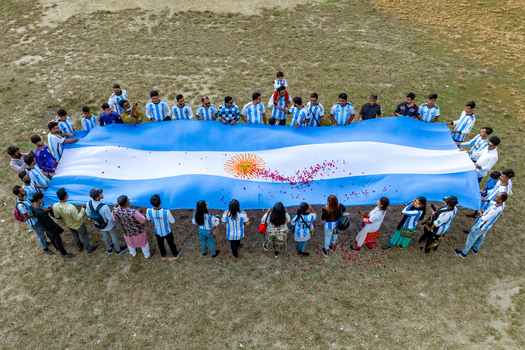 Bogura Bangladesh 02 December 2022 Aerial view of a large group of people holding a giant Argentina flag decorated with flower petals on a grassy field.
