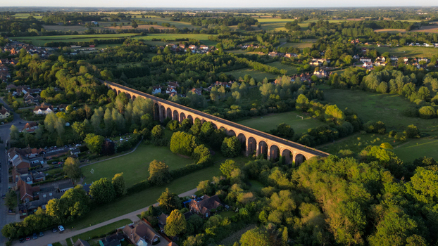 Aerial view of the historic Chappel Viaduct a long brick railway bridge spanning the lush green countryside and trees in Chappel England United Kingdom.