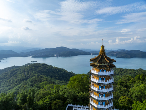 Aerial view of the Ci en Pagoda overlooking the blue waters of Sun Moon Lake surrounded by lush green mountains under a bright sky in Yuchi Township Nantou County Taiwan. Aerial view of the Ci en Pagoda overlooking the blue waters of Sun Moon Lake surrounded by lush green mountains under a bright sky in Yuchi Township Nantou County Taiwan.