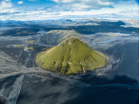 Aerial view of the vibrant green moss covered Maelifell volcano rising from the vast black volcanic sand plains and glacial river patterns in Kirkjubaejarklaustur Skaftarhreppur Iceland. Aerial view of the vibrant green moss covered Maelifell volcano rising from the vast black volcanic sand plains and glacial river patterns in Kirkjubaejarklaustur Skaftarhreppur Iceland.