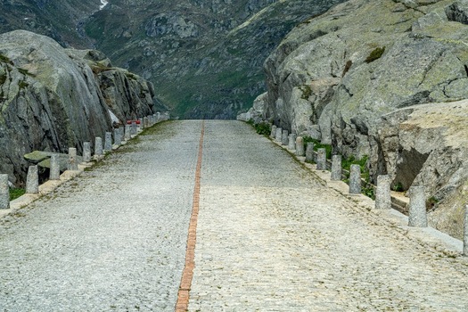 View of the historic cobblestone Tremola road at Sankt Gotthard Pass with stone bollards and rocky mountain slopes in Airolo Ticino Switzerland.