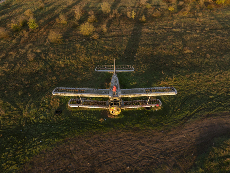 Aerial view of an abandoned biplane resting in a grassy field with a person in an orange jacket standing on the fuselage during golden hour in Bulgaria. Aerial view of an abandoned biplane resting in a grassy field with a person in an orange jacket standing on the fuselage during golden hour in Bulgaria.