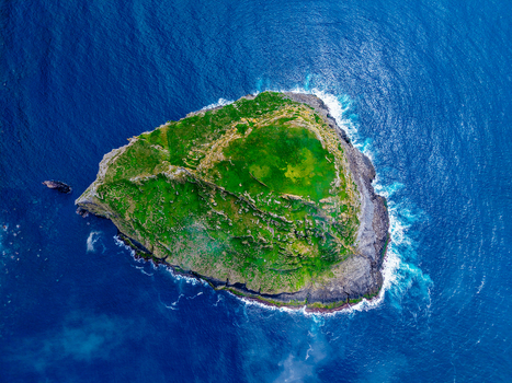 Aerial view of a rugged verdant islet surrounded by the deep blue Atlantic a contrast of textures and tones under the open sky Flores A&ccedil;ores Portugal.