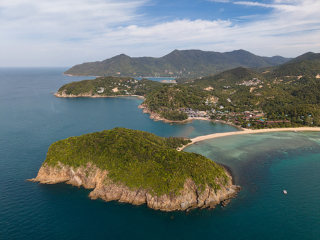 Aerial view of Ko Pha Ngan featuring lush green hills a pristine sandy beach and turquoise waters along the rocky coastline in Ko Pha ngan District Surat Thani Thailand.