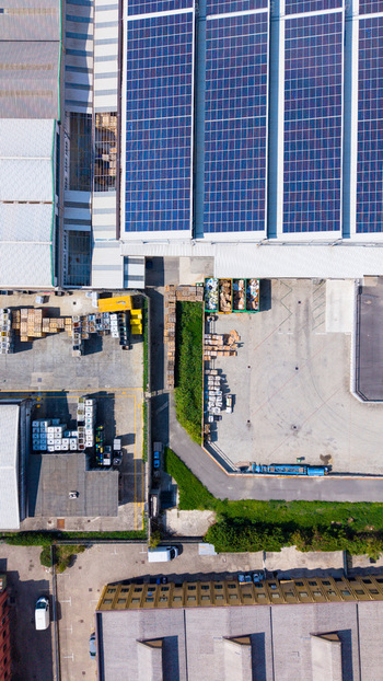 Aerial view of a manufacturing plant featuring large solar panel arrays on the roof an industrial yard with storage pallets and paved parking areas in Milan Lombardy Italy. Aerial view of a manufacturing plant featuring large solar panel arrays on the roof an industrial yard with storage pallets and paved parking areas in Milan Lombardy Italy.