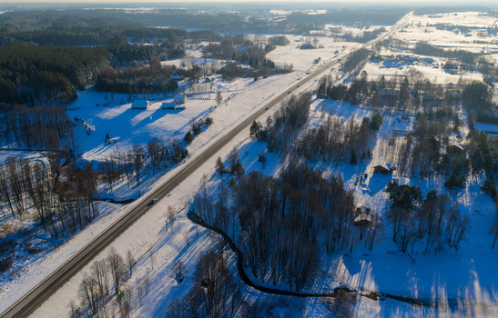 Aerial view of a straight highway passing through snow covered fields and dense forests under bright winter sunlight Lithuania. Aerial view of a straight highway passing through snow covered fields and dense forests under bright winter sunlight Lithuania.