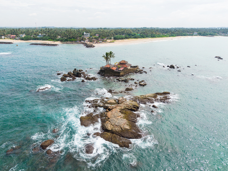 Aerial view of Seenigama Muhudu Dewalaya temple on a rocky island surrounded by turquoise ocean waves and palm trees Peraliya Sri Lanka. Aerial view of Seenigama Muhudu Dewalaya temple on a rocky island surrounded by turquoise ocean waves and palm trees Peraliya Sri Lanka.