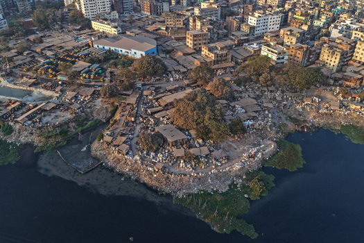 Aerial view of the Buriganga River bank with dense urban settlements informal housing and industrial structures along the water in Dhaka Dhaka Division Bangladesh. Aerial view of the Buriganga River bank with dense urban settlements informal housing and industrial structures along the water in Dhaka Dhaka Division Bangladesh.