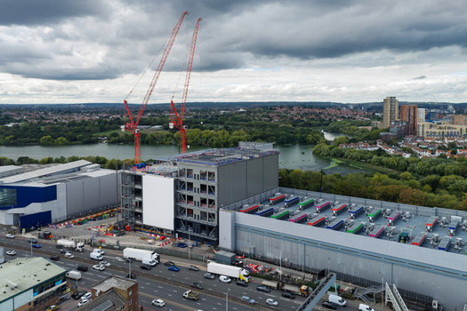 Aerial view of a large data center construction site featuring two tall red cranes industrial buildings with rooftop cooling units and busy traffic in the United Kingdom.