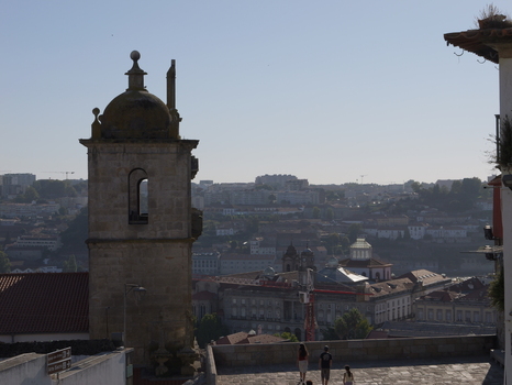 View of a historic stone church tower overlooking the cityscape of Porto with people walking on a stone terrace in the foreground under a clear sky in Porto Porto District Portugal. View of a historic stone church tower overlooking the cityscape of Porto with people walking on a stone terrace in the foreground under a clear sky in Porto Porto District Portugal.