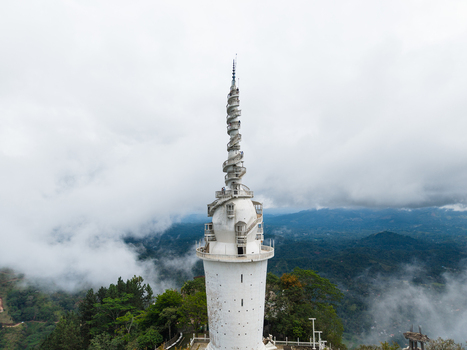 Aerial view of Ambuluwawa Tower a unique spiral structure rising above misty green hills and dense forests under a cloudy sky Gampola Central Province Sri Lanka. Aerial view of Ambuluwawa Tower a unique spiral structure rising above misty green hills and dense forests under a cloudy sky Gampola Central Province Sri Lanka.